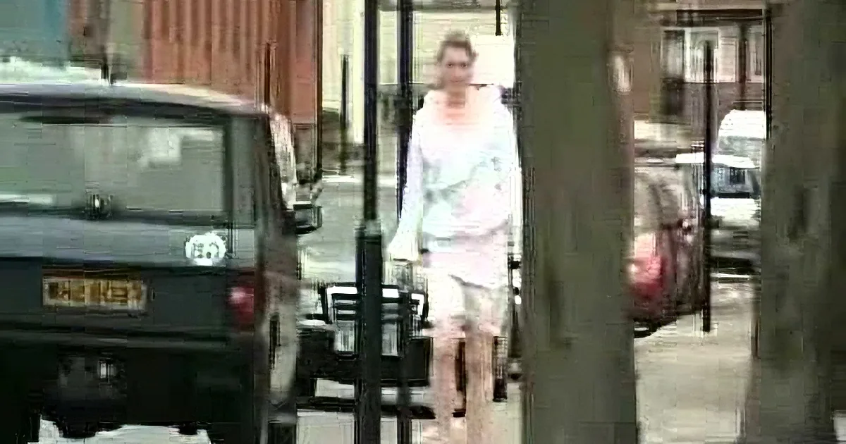 A person in a white outfit walks on a sidewalk, partially obscured by trees and parked cars.