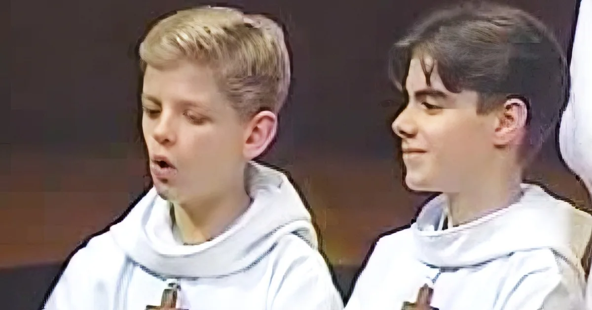 Two young boys in white robes with crosses, standing close, possibly in a religious setting.
