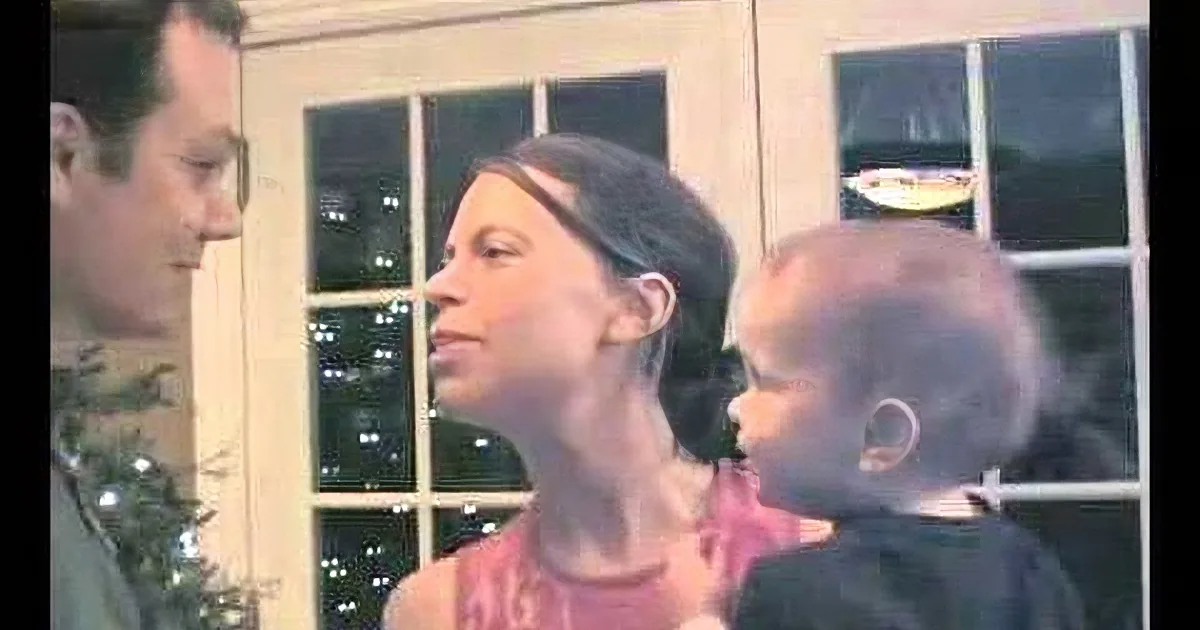 A woman with tattoos on her neck and shoulders is speaking to a man in a festive setting with Christmas lights.
