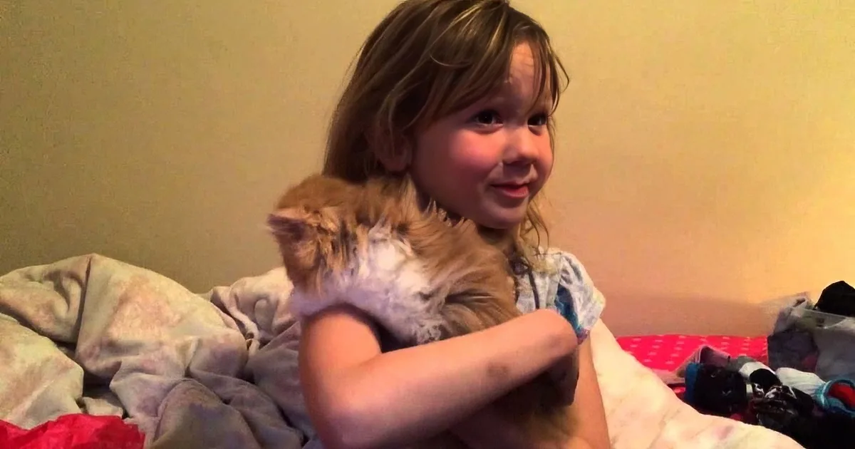 A smiling child hugs a stuffed animal on a bed with colorful blankets and toys.