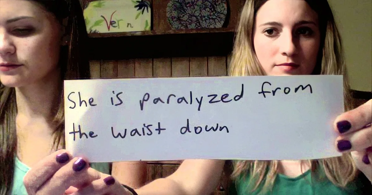 A woman holds a sign stating "She is paralyzed from the waist down."