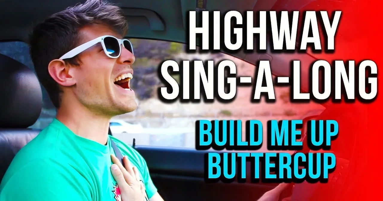 A man in a car wearing sunglasses and a green shirt is singing along to "Build Me Up Buttercup."