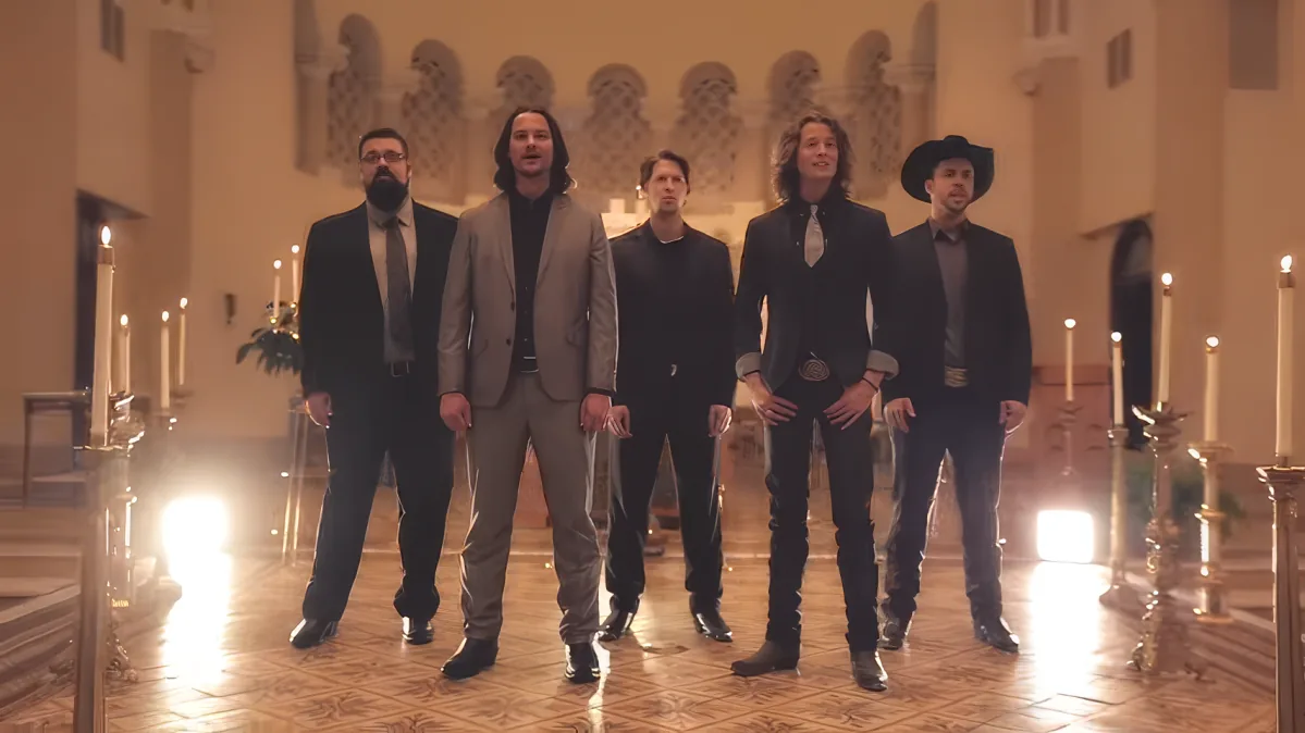 Five men in formal attire stand in a church with candles and ornate architecture.