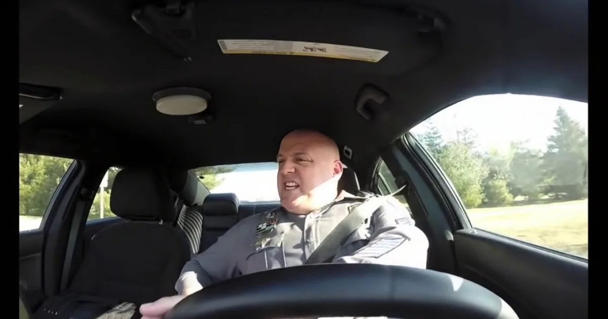 A man in a uniform drives a car, smiling, with a passenger in the back seat.