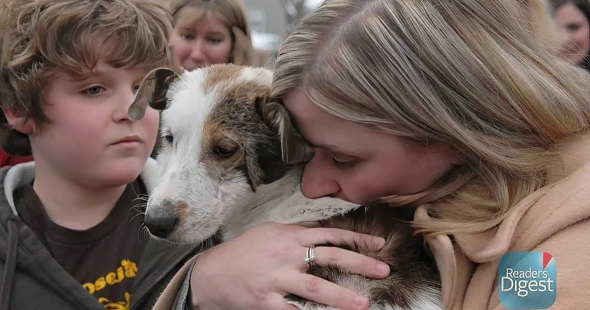 A woman hugs a dog while a boy watches, both in a crowd.