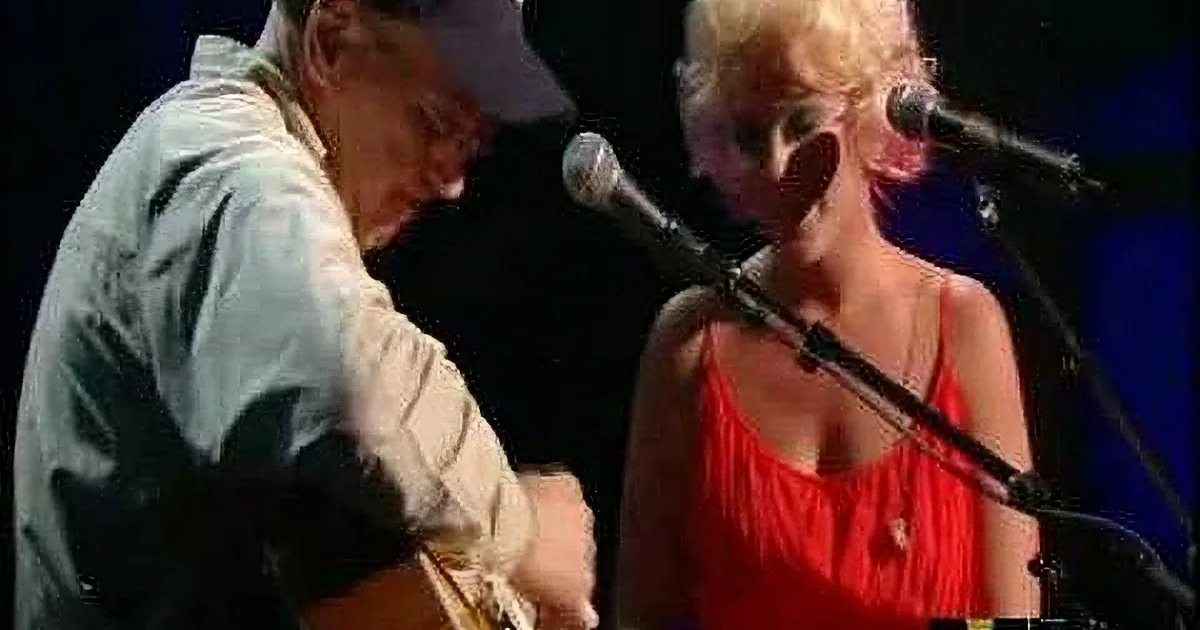 A man in a cap plays guitar while a woman in a red dress sings into a microphone.