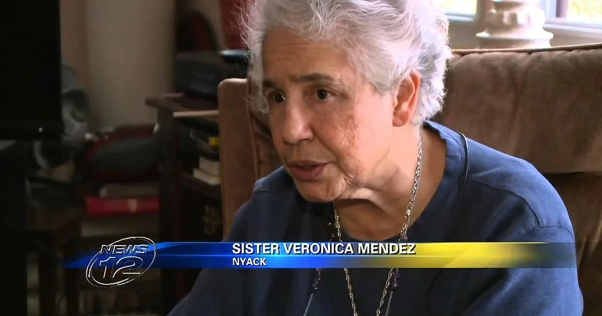 An elderly woman in a blue shirt is being interviewed, with a name tag identifying her as Sister Veronica Mendez from Nyack.