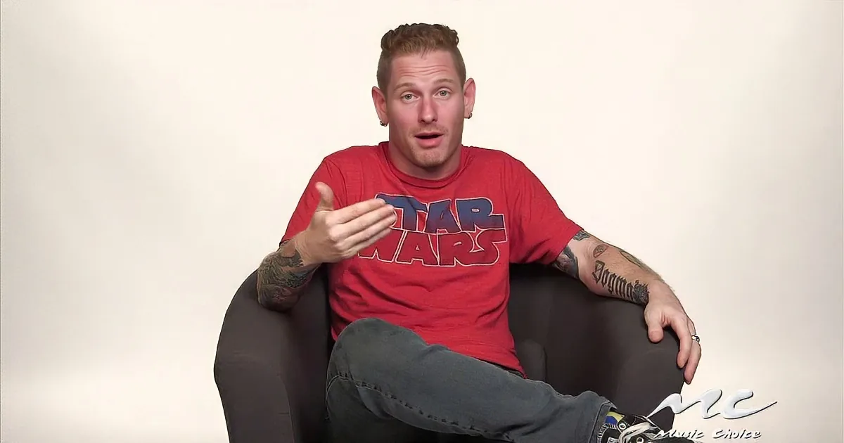 A man in a red Star Wars shirt sits in a chair, gesturing with his hand, tattoos visible.