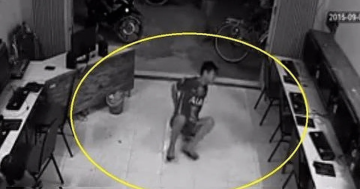 A man in a black shirt and shorts is kneeling on the ground, surrounded by a yellow circle in a security camera view.