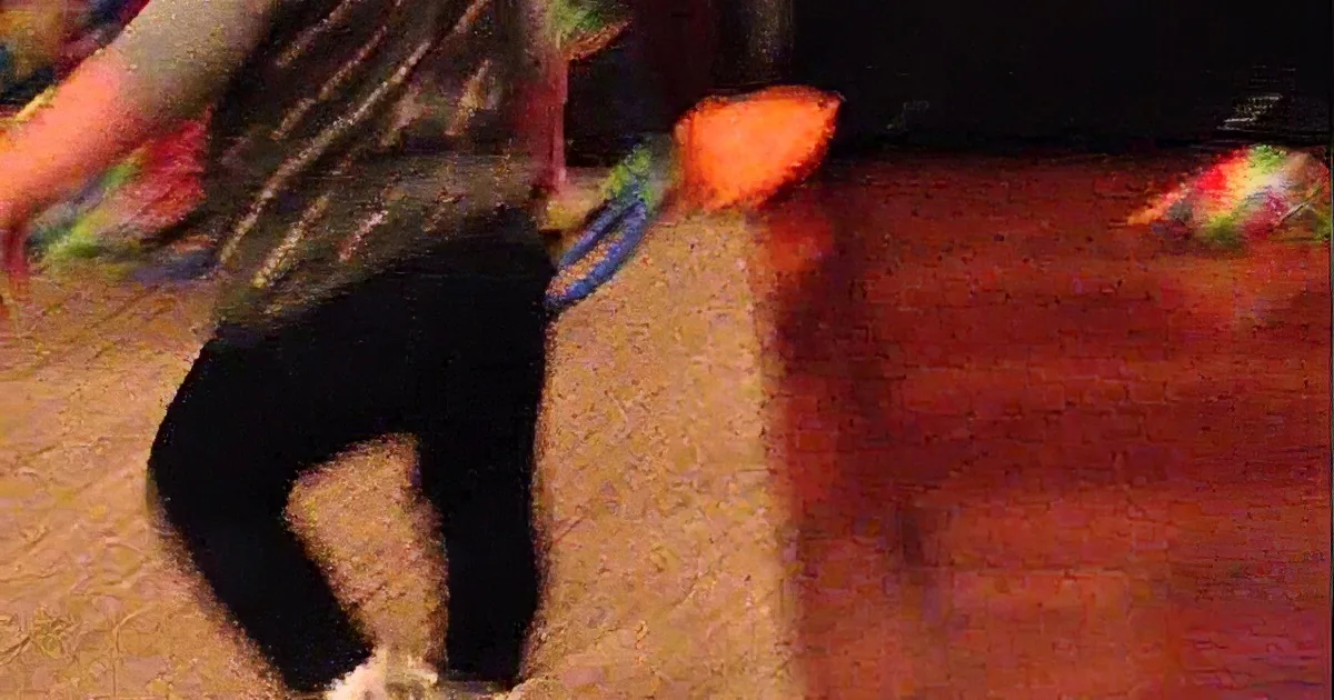 A person in motion, wearing a patterned shirt and dark pants, holding a blue object, with a blurry orange item and...