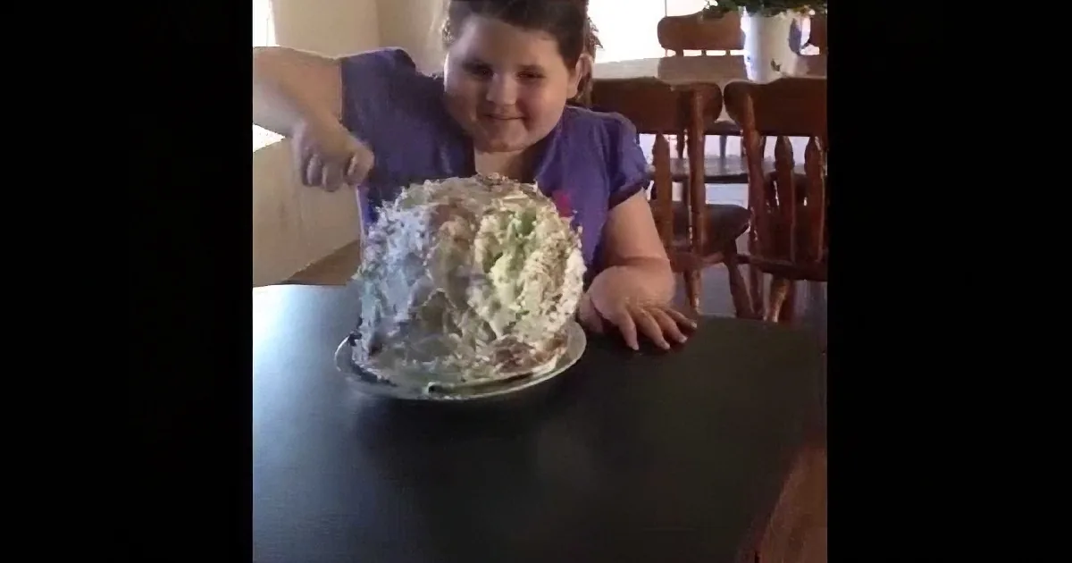 A child sits at a table, holding a large bowl of shredded food, possibly a salad or coleslaw.