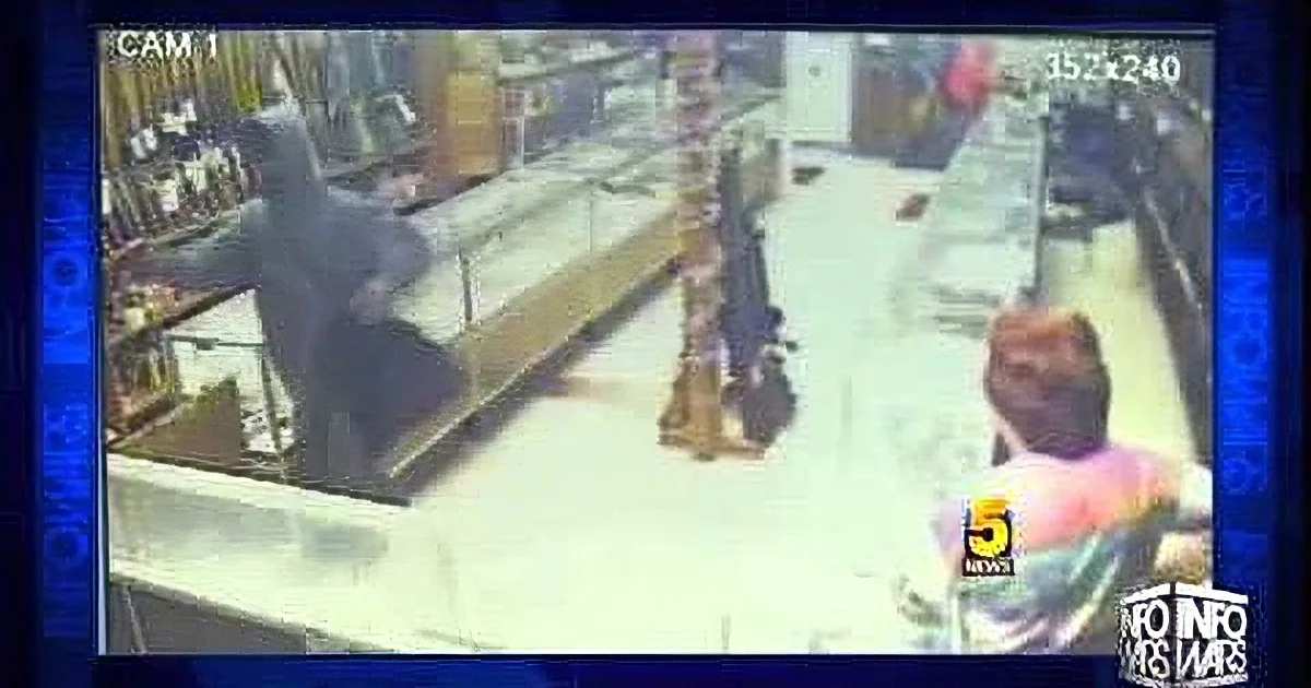 A person in a hoodie is standing behind a counter in a store, possibly robbing it.