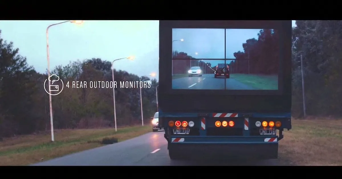 A truck displays a rear-view monitor showing traffic on a highway at dusk.