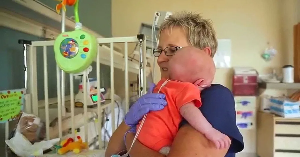A person holds a baby in a hospital setting, surrounded by medical equipment and toys.