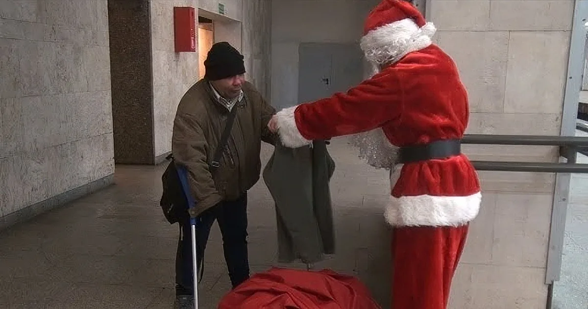 A person dressed as Santa Claus is handing a bag to another individual in a hallway.
