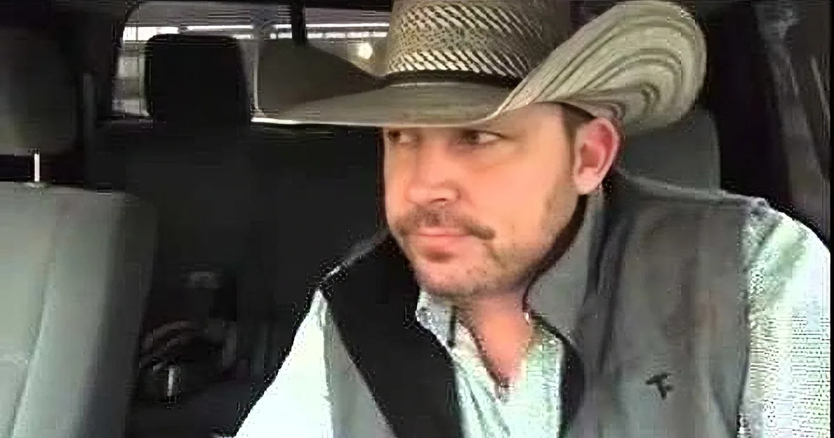 A man wearing a cowboy hat and vest is seated in a car, looking to the side.