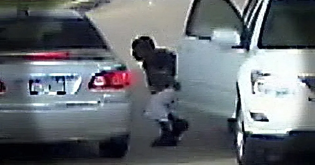 A person is seen in a parking lot, leaning against a white car, with another car parked nearby.
