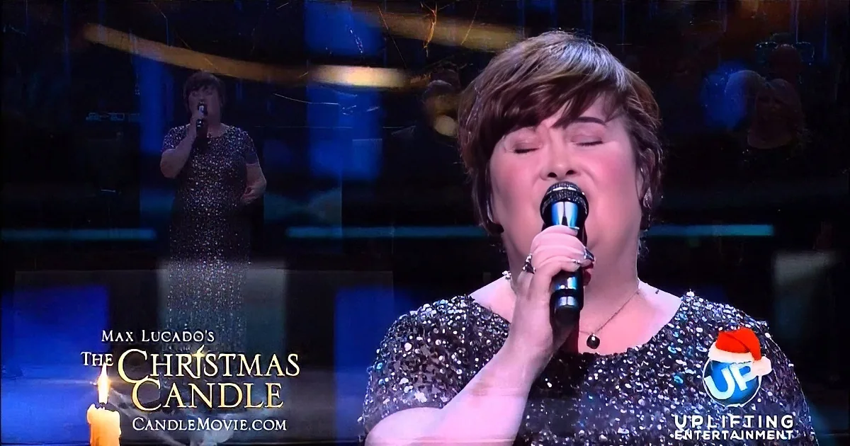 A woman in a glittery dress sings into a microphone on stage, with a candle and Christmas-themed text in the foreground.