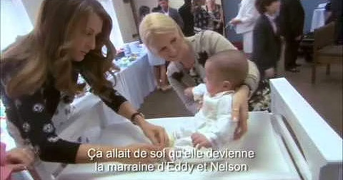 Two women interact with a baby, one holding a bottle, in a social setting.