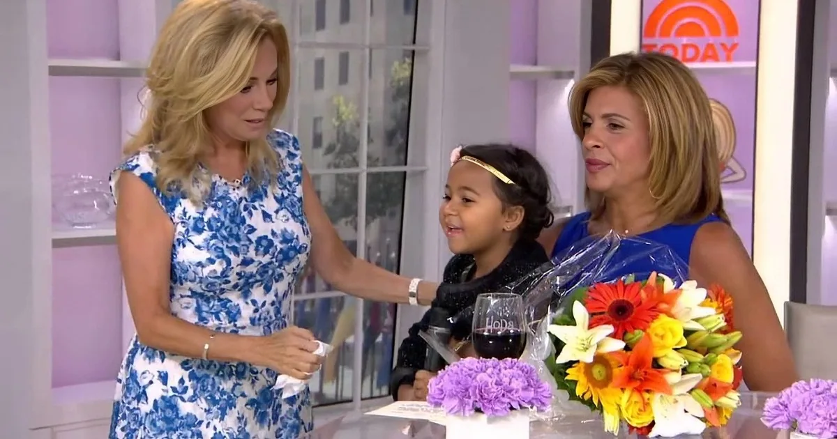 Two women and a child smile at a bouquet of flowers on a TV show set.