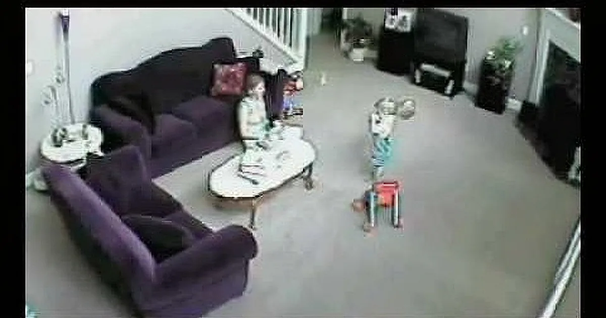 A child stands on a toy box in a living room with purple furniture and a staircase in the background.