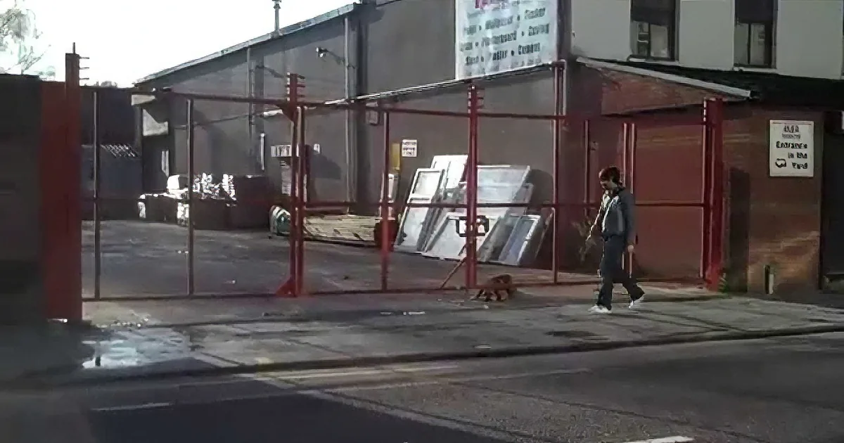 A person walks past a red gate with a sign indicating entrance is in the yard.