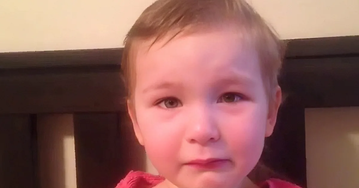 A young child with short hair and a red garment is looking directly at the camera.
