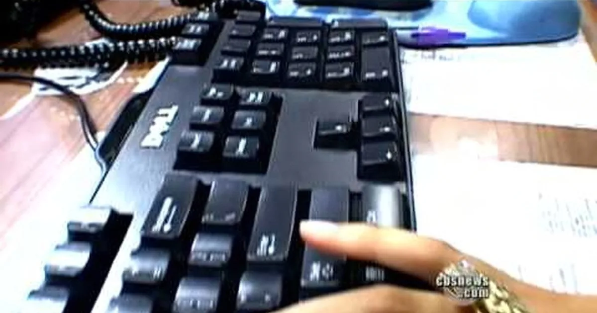 A Dell keyboard is shown with a finger pressing a key, surrounded by a desk with papers and a phone.
