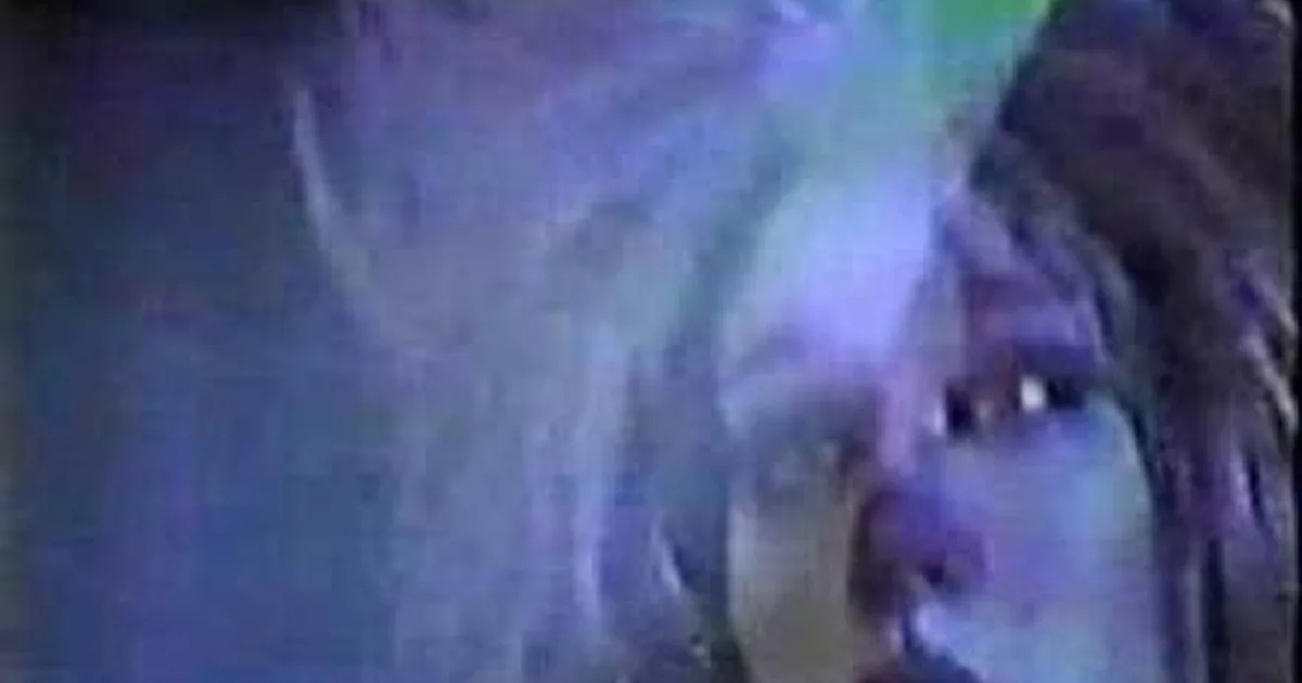 A close-up of a person with dreadlocks, their face partially obscured by a blurred, light-colored object.