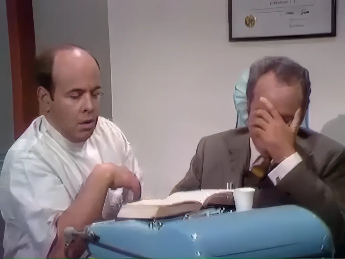 A man in a white shirt is reading a book, while another man in a suit covers his face, possibly in frustration or...