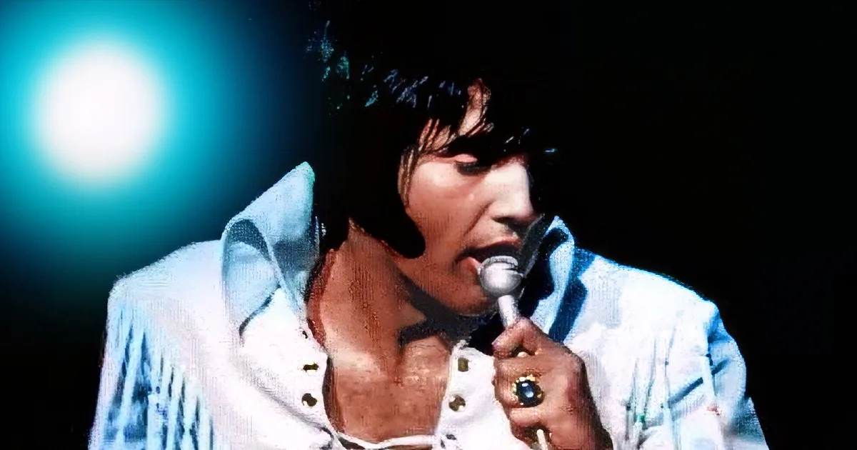 A man in a white suit holds a microphone, singing under bright stage lights.