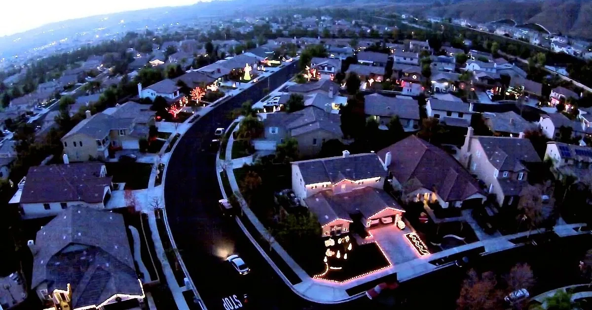 Aerial view of suburban neighborhood with houses lit up at dusk, featuring a prominent house with festive lights.
