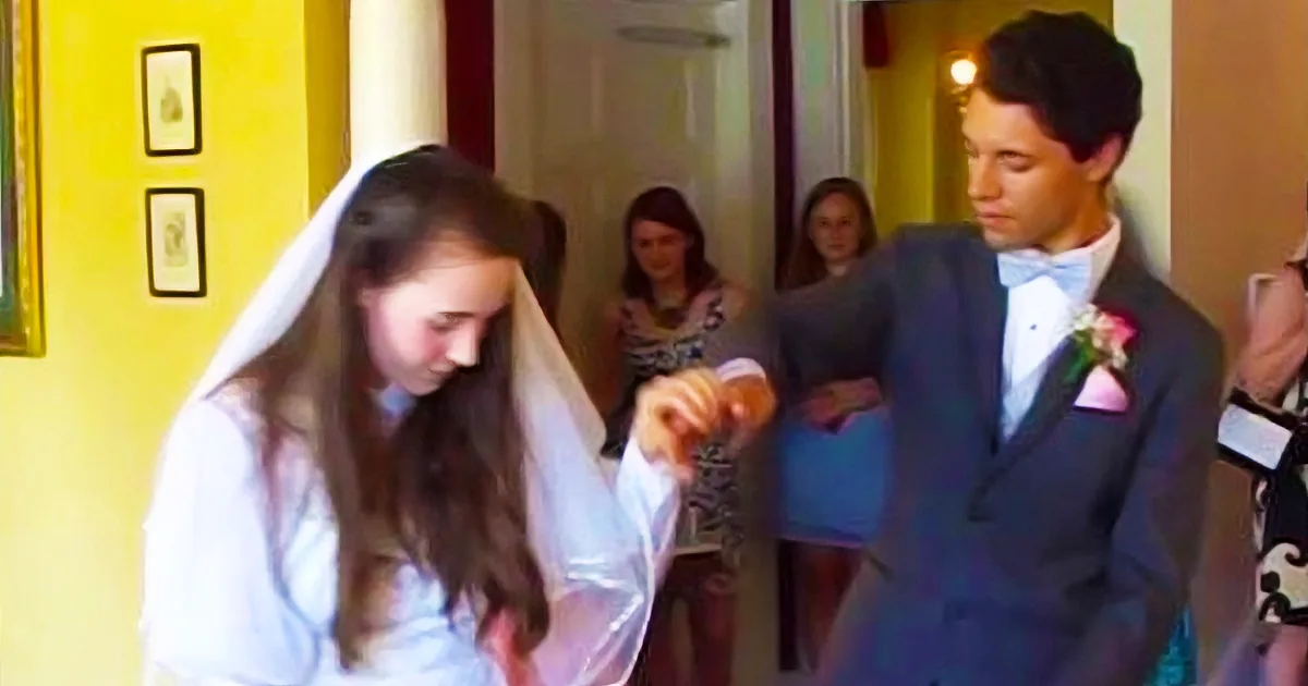 A bride and groom are dancing, the bride is wearing a white dress and veil, and the groom is in a tuxedo with a pink...