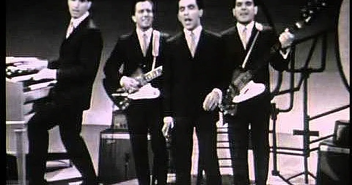 Four men in suits play guitars and sing on stage, black and white.