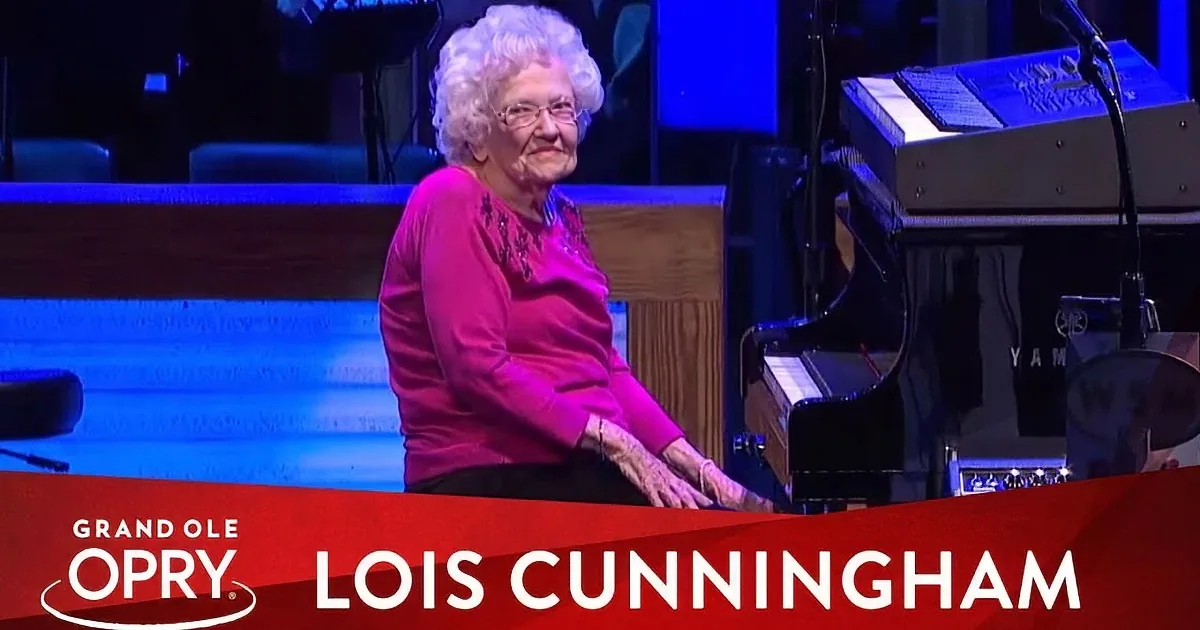 An elderly woman in a pink top plays piano on stage at the Grand Ole Opry.