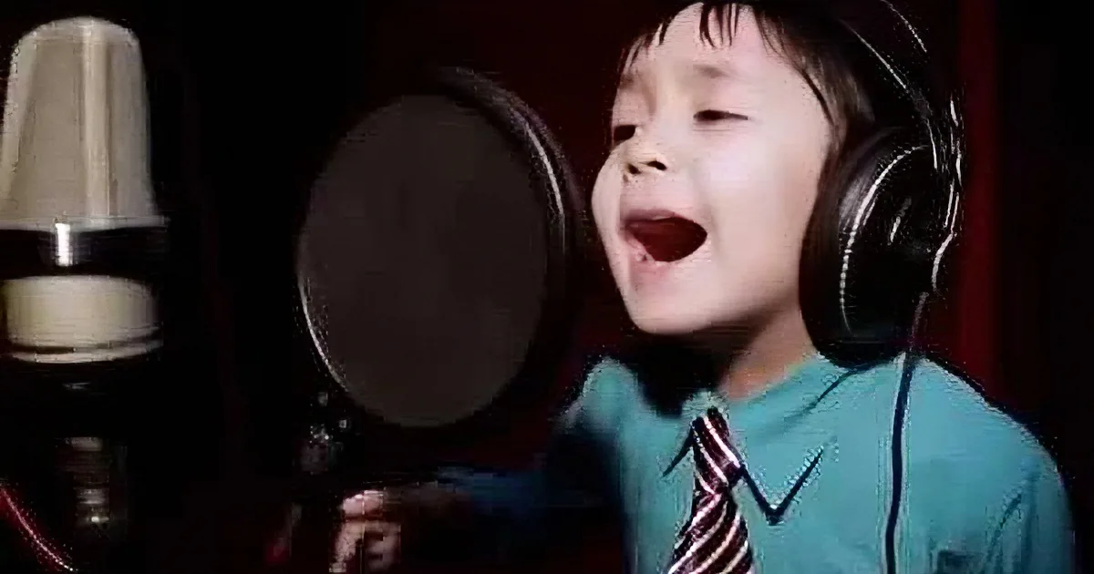 A young boy wearing headphones sings into a microphone in a recording studio.