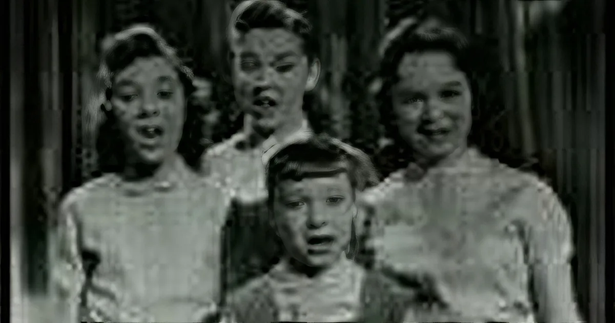A group of children, possibly from a vintage film, are singing or speaking in unison.