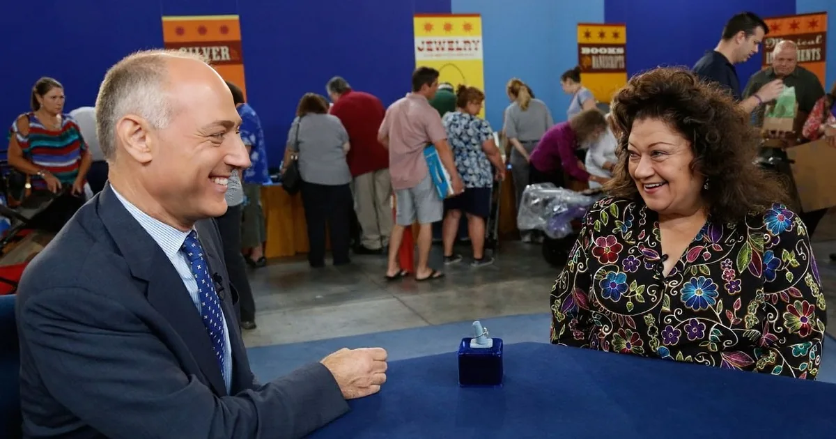A man in a suit and a woman in a floral blouse are smiling at each other at a table.