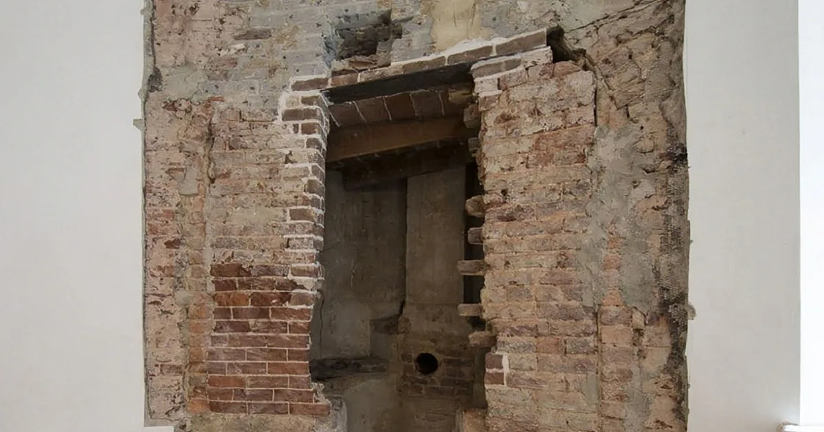 A partially demolished brick wall with exposed mortar and a hole in the center.