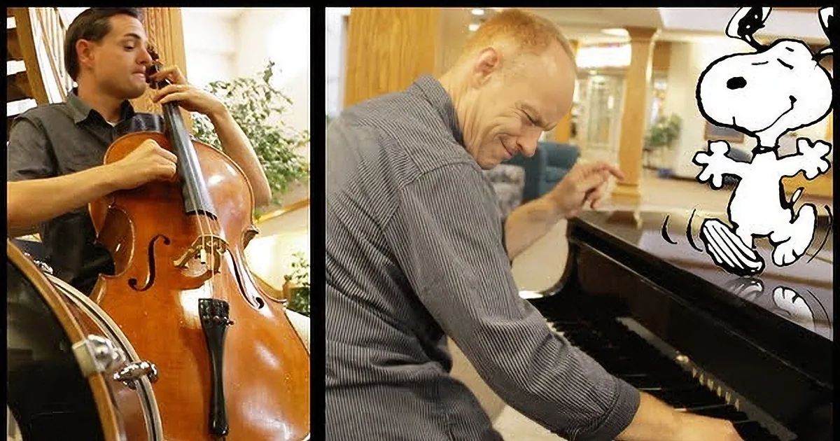 A man plays a cello while another man plays a piano, with a Snoopy cartoon character in the background.