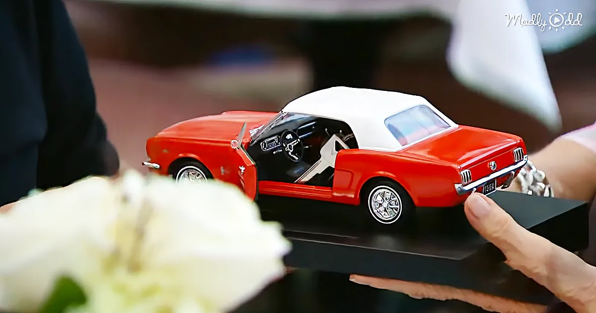 A red and white vintage car model with open doors is displayed on a black stand.
