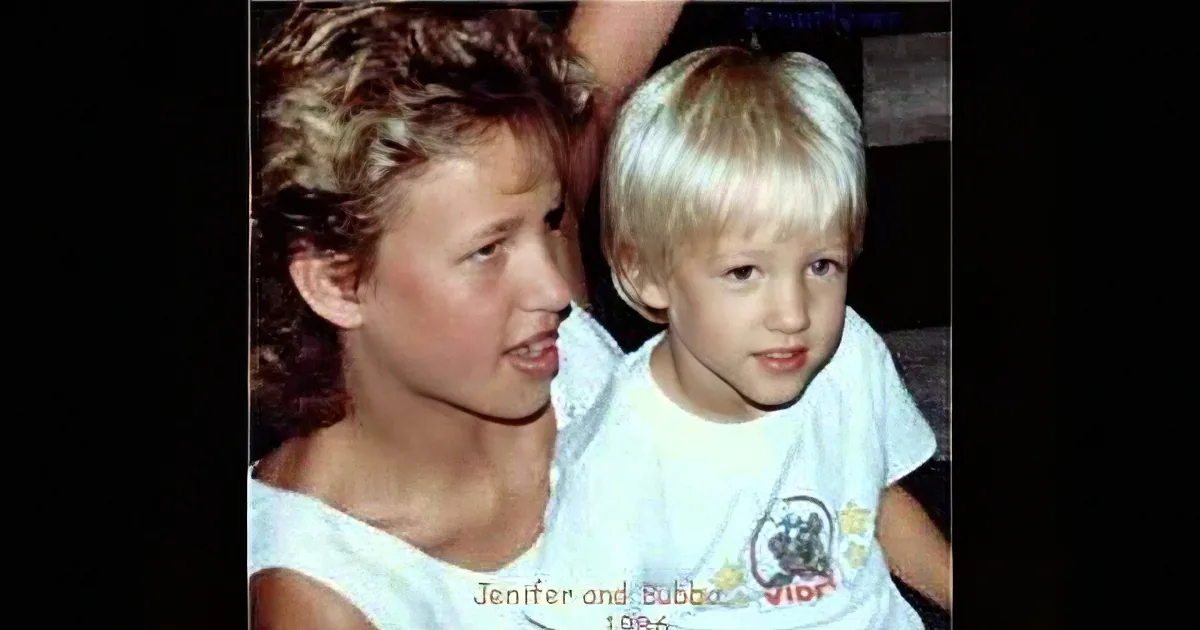 A young child with blonde hair and a white shirt is being held by a woman with short, curly hair.