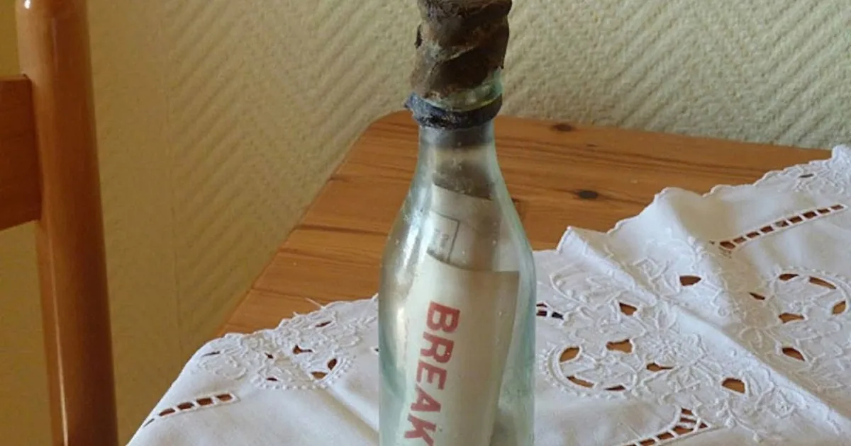A glass bottle with a twisted top sits on a lace doily atop a wooden table.