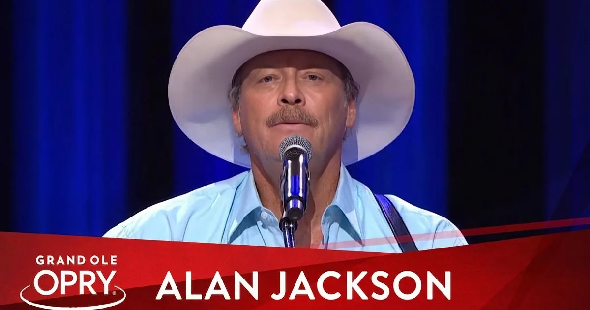 Alan Jackson in a white cowboy hat sings at the Grand Ole Opry.