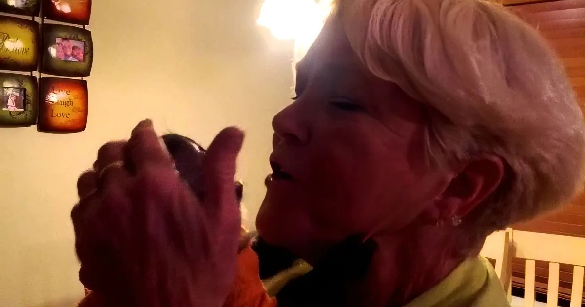 An elderly woman with short gray hair is holding and examining a small object in her hands.
