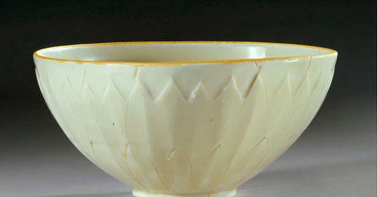 A white ceramic bowl with intricate leaf patterns and a yellow rim sits on a neutral surface.