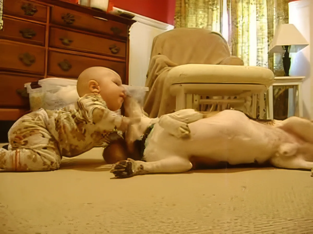 A baby in pajamas lies on a carpeted floor, reaching out towards a beige chair.