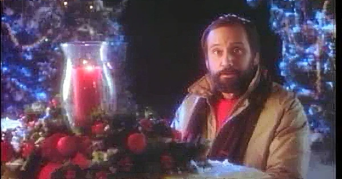 A man with a beard sits in front of a Christmas tree, surrounded by festive decorations and a lit candle.