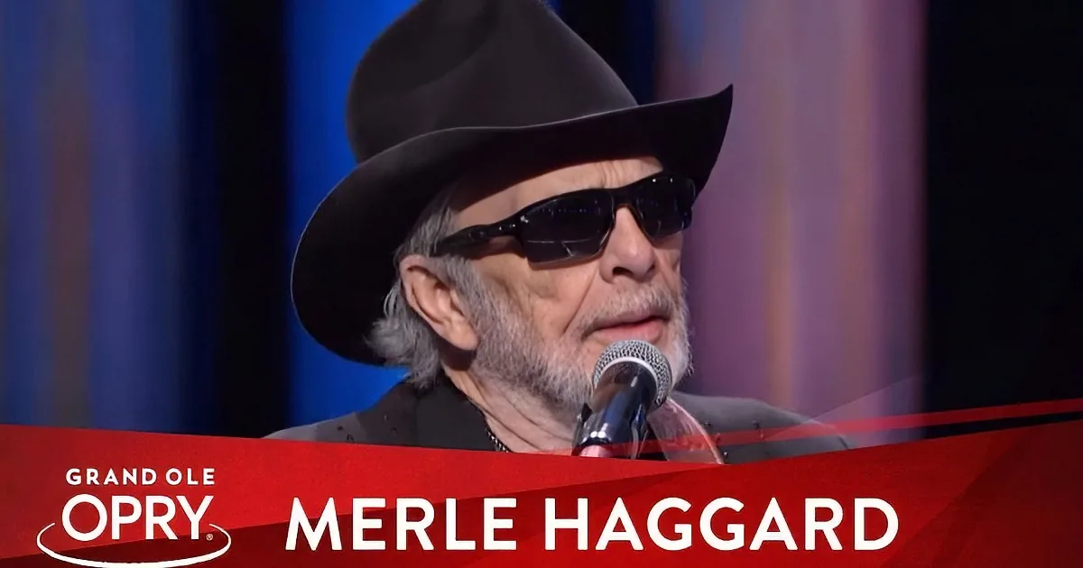 Merle Haggard, wearing a black hat and sunglasses, sings into a microphone at the Grand Ole Opry.