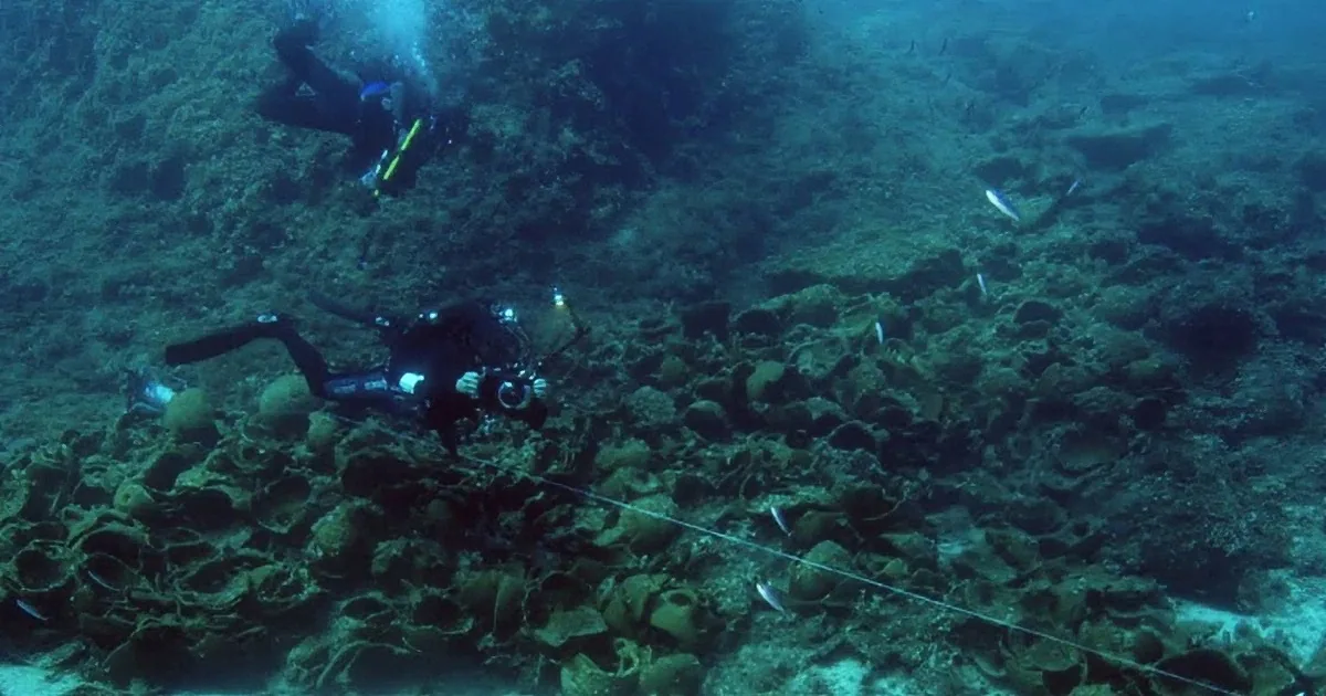 Two scuba divers explore a coral reef, surrounded by marine life and underwater structures.